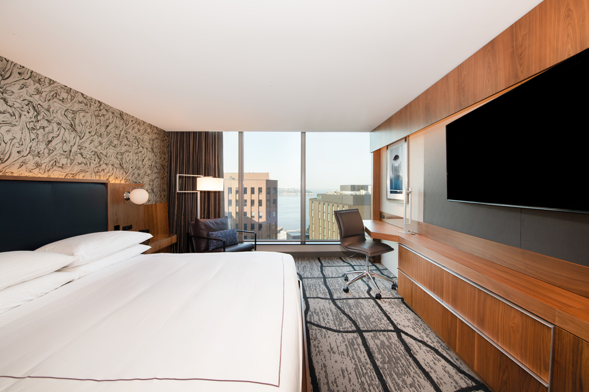 A hotel room with a king-size bed, desk, chair, and city view.